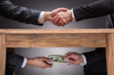Businesspeople Shaking Hands And Taking Bribe Under Table