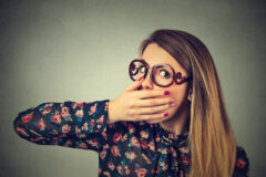 scared young woman in glasses covering with hand mouth