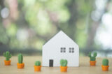 Close up of wooden mini house toy with mini cactus plant pot on wooden table.