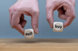 Hands are holding two cubes with the words "sell" and "buy". One hand rises the cube with the word "buy".