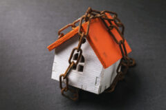 A toy house wrapped in a chain on a dark background. The concept of the arrest of property for tax evasion