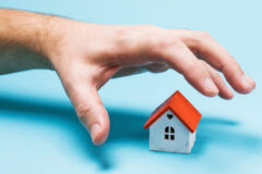 A hand reaches for a toy house. The concept of fraud and theft